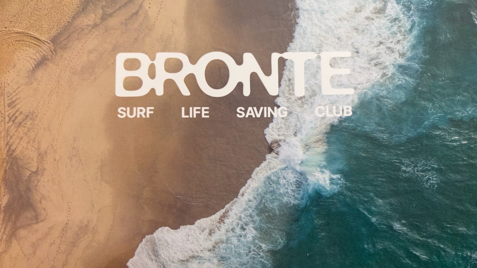 The masthead on the cover of Bronte Surf Life Saving Club's annual report, set over an aerial photograph of a wave breaking along the shoreline